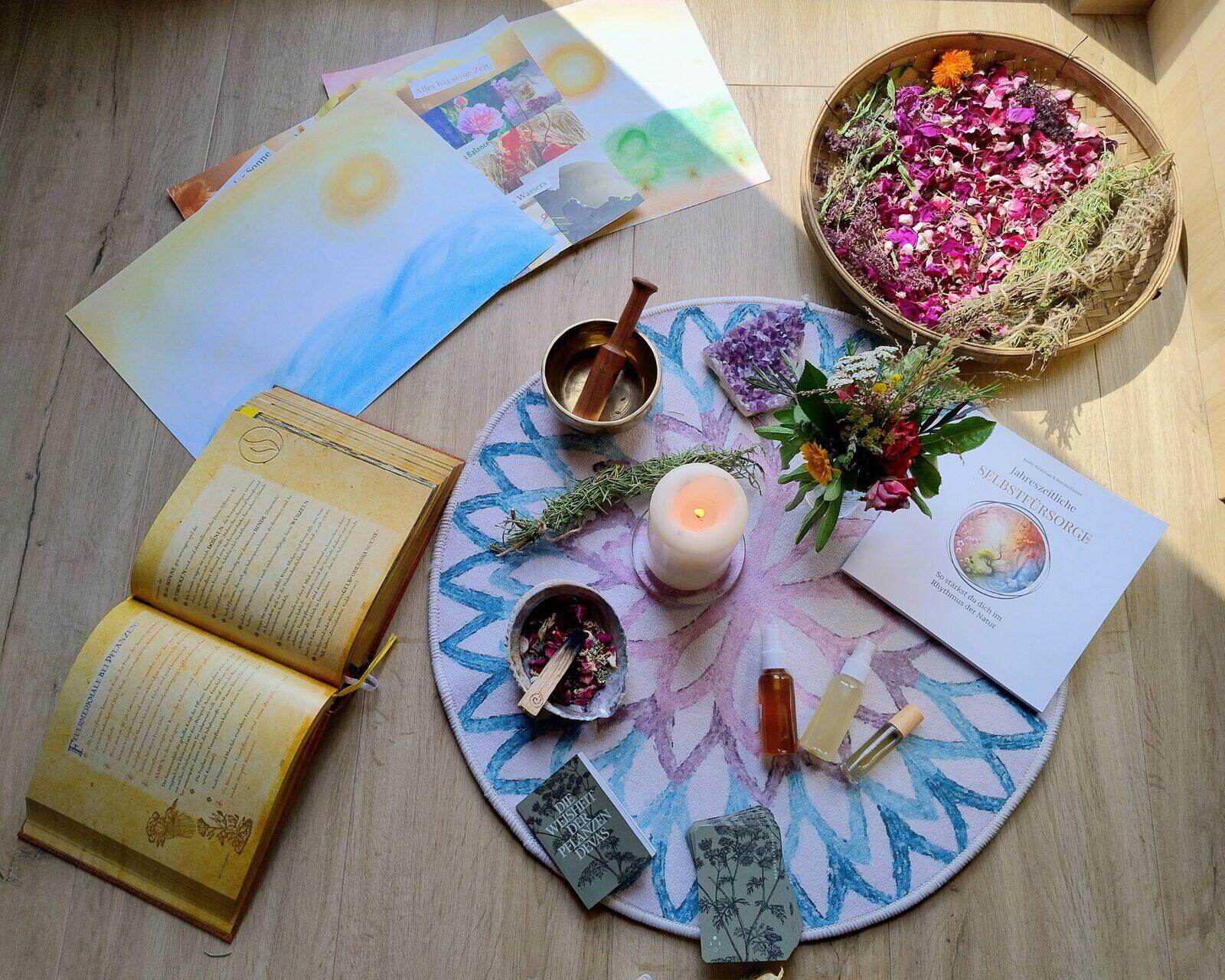 Mandala-Anordnung mit Kerze, Klangschale, Blüten, Ölen und dem Buch „Jahreszeitliche Selbstfürsorge“ als Sinnbild für die 5 Säulen im Gleichgewicht