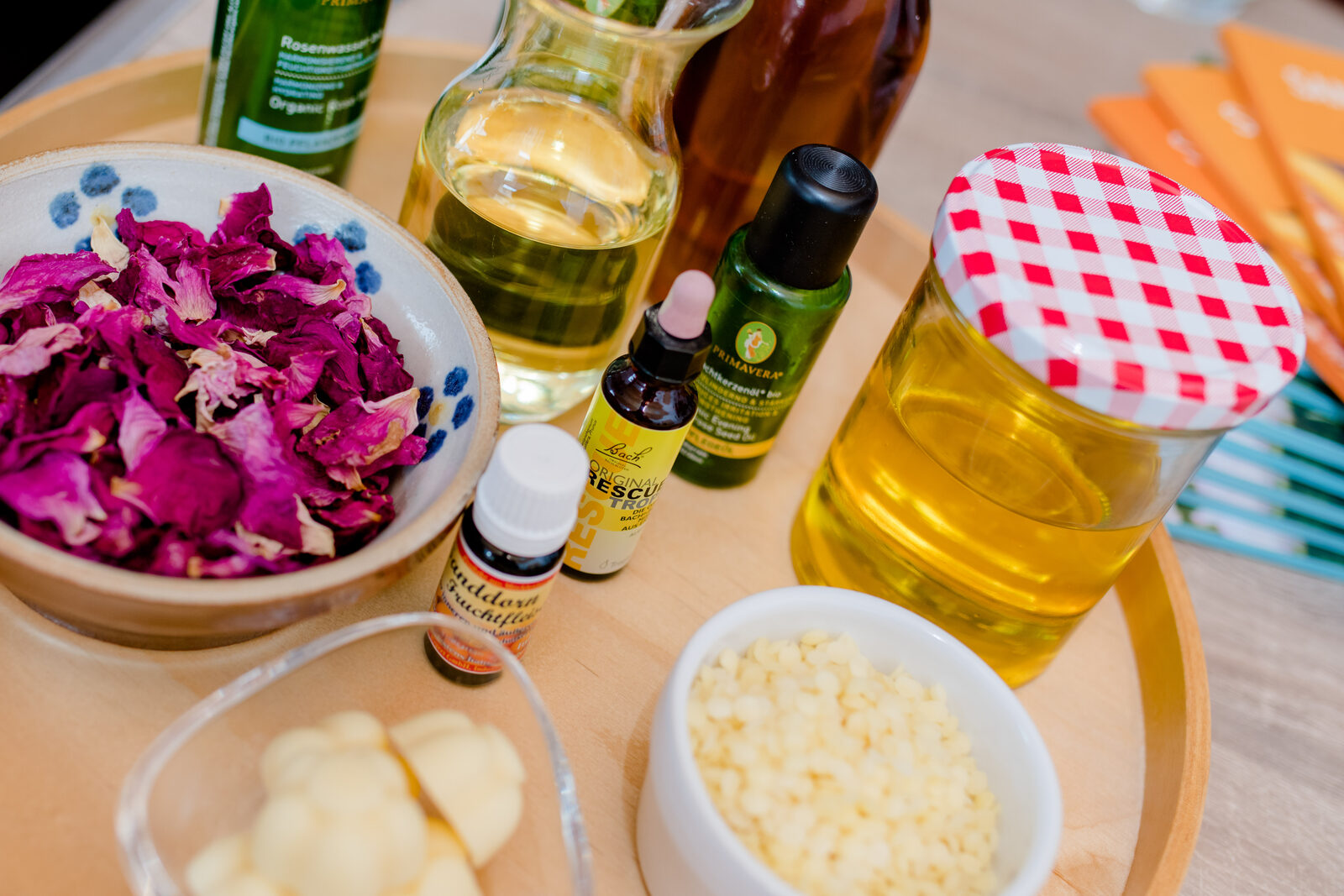 Zutaten für selbstgemachte Naturkosmetik: Rosenblätter, Öle und Bienenwachs auf einem Holztablett
